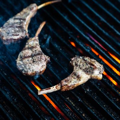 Three lamb chops grilling over hot charcoal grate flames.