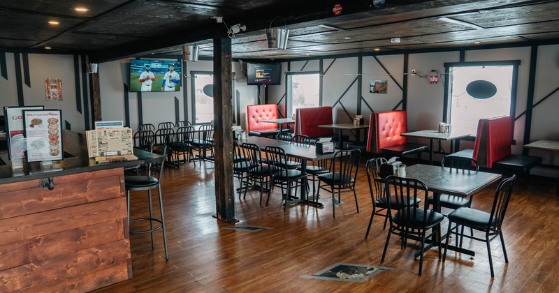 Cozy, rustic bar interior with wooden flooring, metal chairs, and red booths