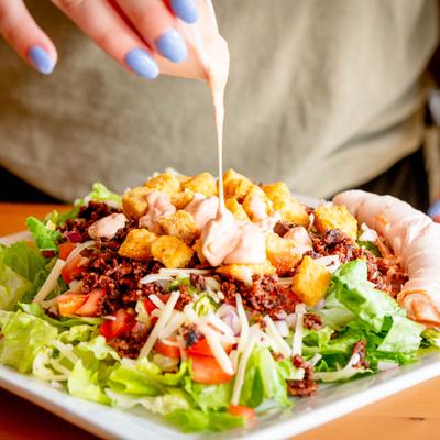 Sauce being drizzled over a Caesar salad.