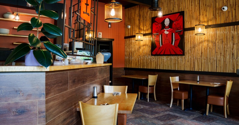 Interior of a restaurant with wooden counter, vibrant red artwork, and bamboo paneling
