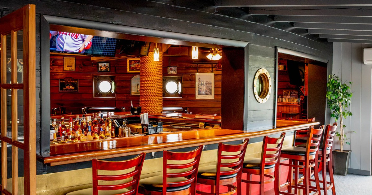 The interior of a bar featuring a long wooden counter, high-backed chairs