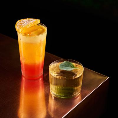 Garibaldi cocktail and Book of Wei cocktail sit on a copper bar counter surface.