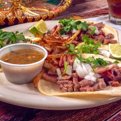 Plate of Street tacos topped with onion and cilantro, served with a dipping sauce.