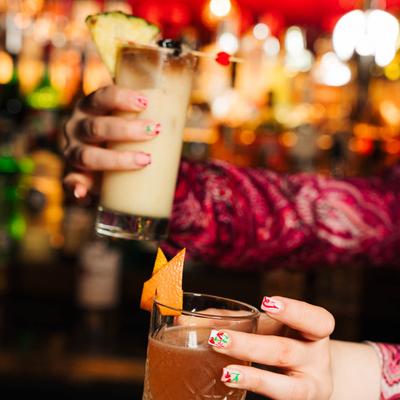 A bartender with colorful nail art holding two cocktails.