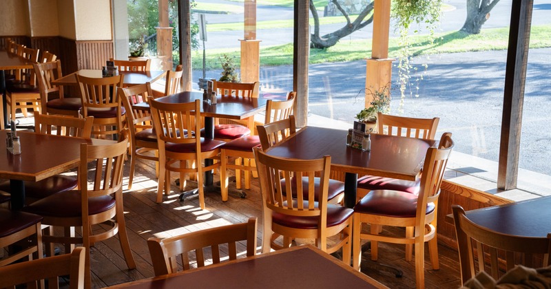 Interior of a cozy restaurant with wooden tables and chairs, red padded seats