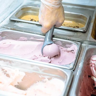 Ice cream being scooped up from ice cream display counter.