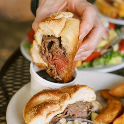 Roast beef sandwich held above dipping sauce.