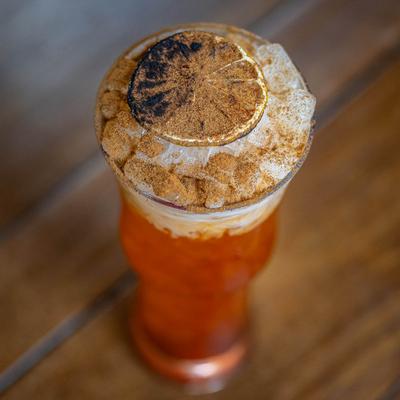A craft red cocktail with crushed ice, garnished with a charred lime wheel.