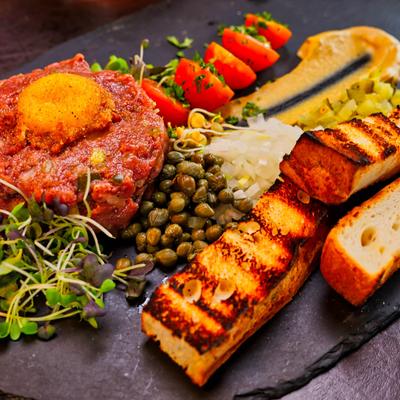 Beef tartare topped with a seasoned egg yolk served with capers, grilled bread, and tomatoes.