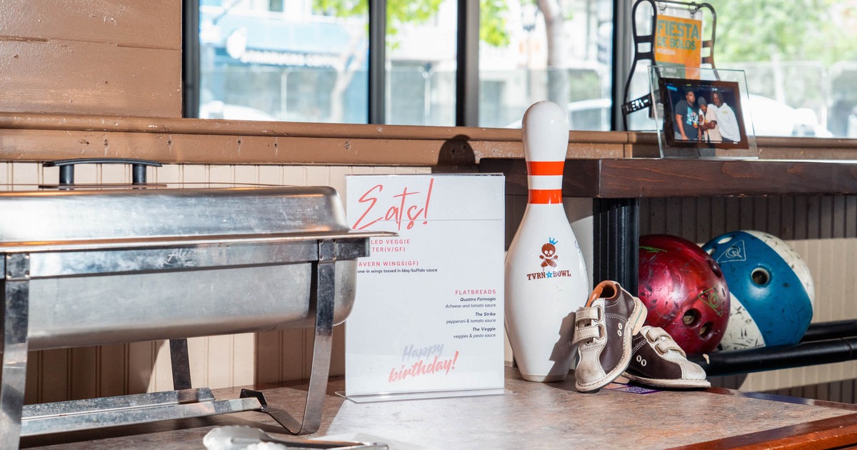 Buffet chafing dish, bowling pin, baby shoes, and bowling balls on a table with a menu
