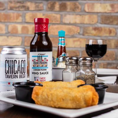 Egg rolls served with dipping sauces, accompanied with canned beer and a bottle of sauce.