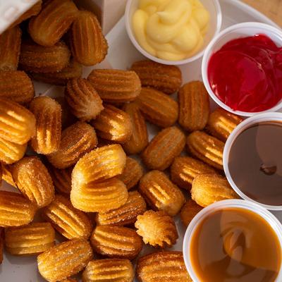 Small churros on a plate with four dipping sauces: yellow, red, chocolate, caramel.