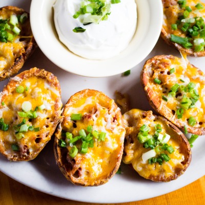 Potato skins topped with cheese and green onion plated with a side of sour cream