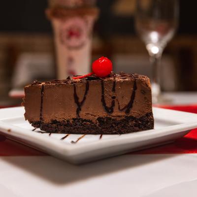 Chocolate cake slice topped with chocolate sauce drizzle and a maraschino cherry.