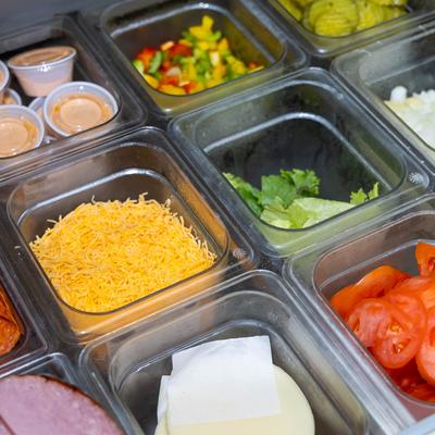 Sandwich station compartments with various toppings.
