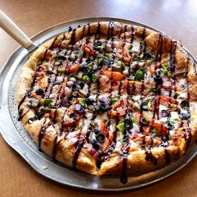 Veggie pizza with balsamic glaze drizzle on a metal tray.