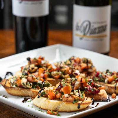 A plate with bruschetta served on a wooden table, with wine bottles in the background.