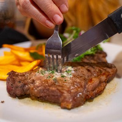 Person cutting into a grilled steak served with french fries and a small side salad.