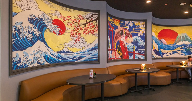 Cozy seating area with curved upholstered seats, round tables and Japanese-style murals on the walls