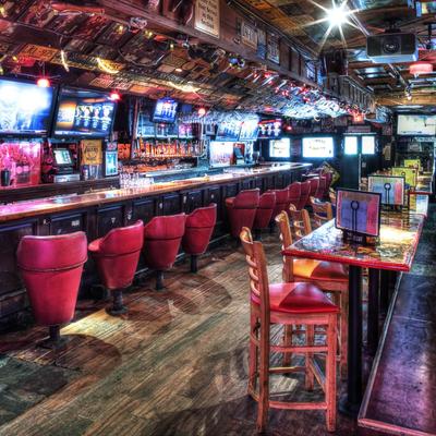 Lively bar with wooden floors, red cushioned stools, and vibrant lights