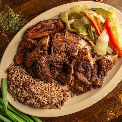 Quarter dark chicken with sauce, served with cabbage and rice and peas.