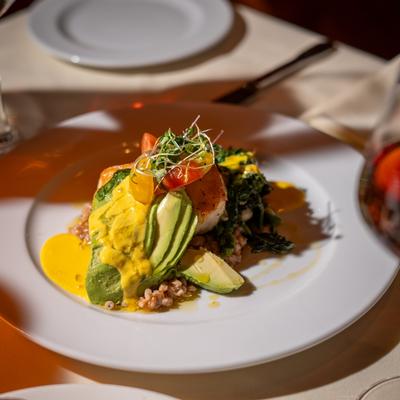 Avocado salad with grains, cherry tomatoes, microgreens, and a vibrant yellow sauce.