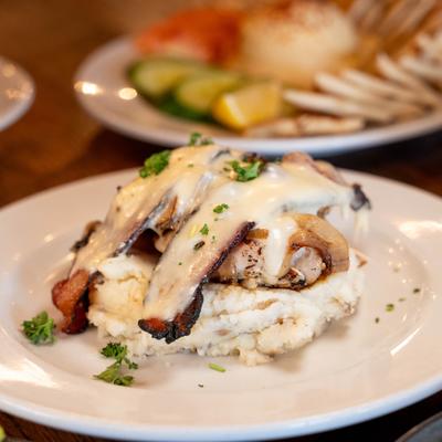 A plate of mashed potatoes topped with grilled meat and creamy sauce, garnished with chopped herbs.