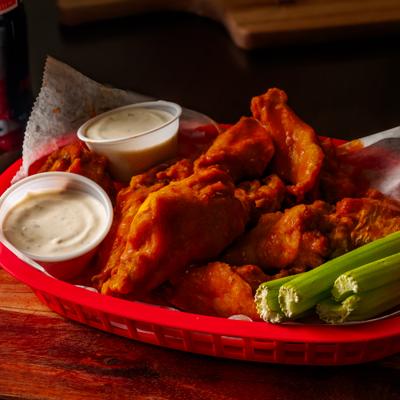 A basket of buffalo wings with celery sticks and ranch dipping sauce.