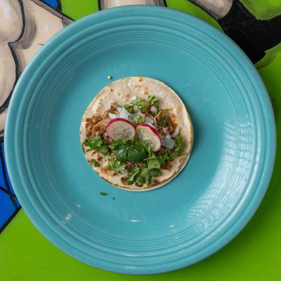 Street taco topped with cilantro, onion, and radish slices on a blue plate.