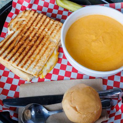 Grilled cheese and a bowl of lobster bisque soup served with a bread roll.
