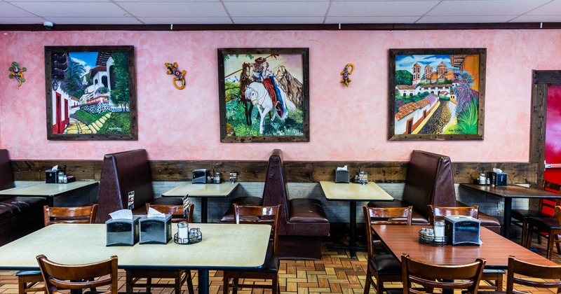 Interior of a restaurant with pink walls, three framed paintings, and dining tables with booths and chairs