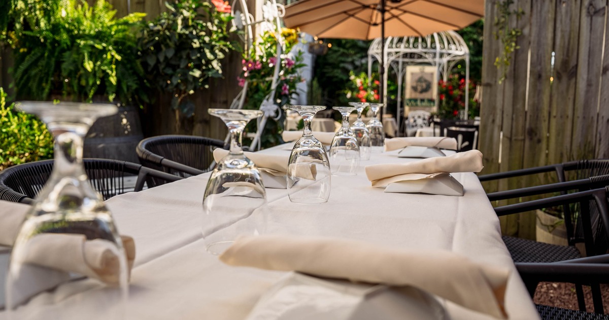 Outdoor dining table with white cloth, inverted wine glasses, and napkins in a garden setting