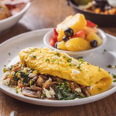 Vegetable omelet topped with feta cheese and herbs, served with a fruit salad