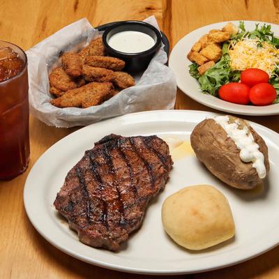 Sirloin served with a bread roll and baked potato, beside a salad, fried mushrooms and a drink.