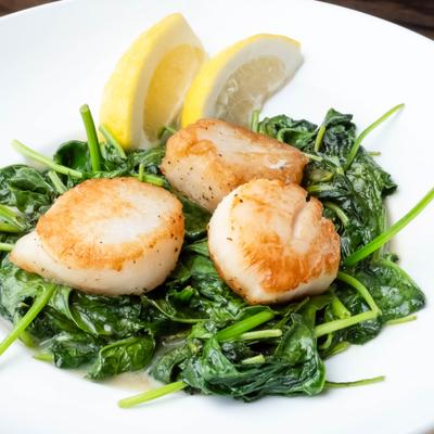 Pan-seared scallops served on a bed of sautéed spinach with lemon wedges.
