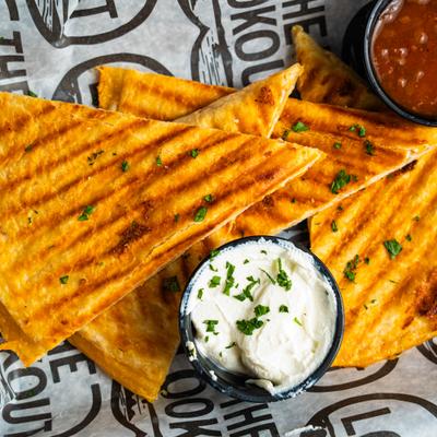 Chicken quesadilla served with salsa and sour cream on branded paper, close-up.