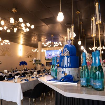 Banquet room set for dining, with a large blue birthday cake displayed with blue bottles.