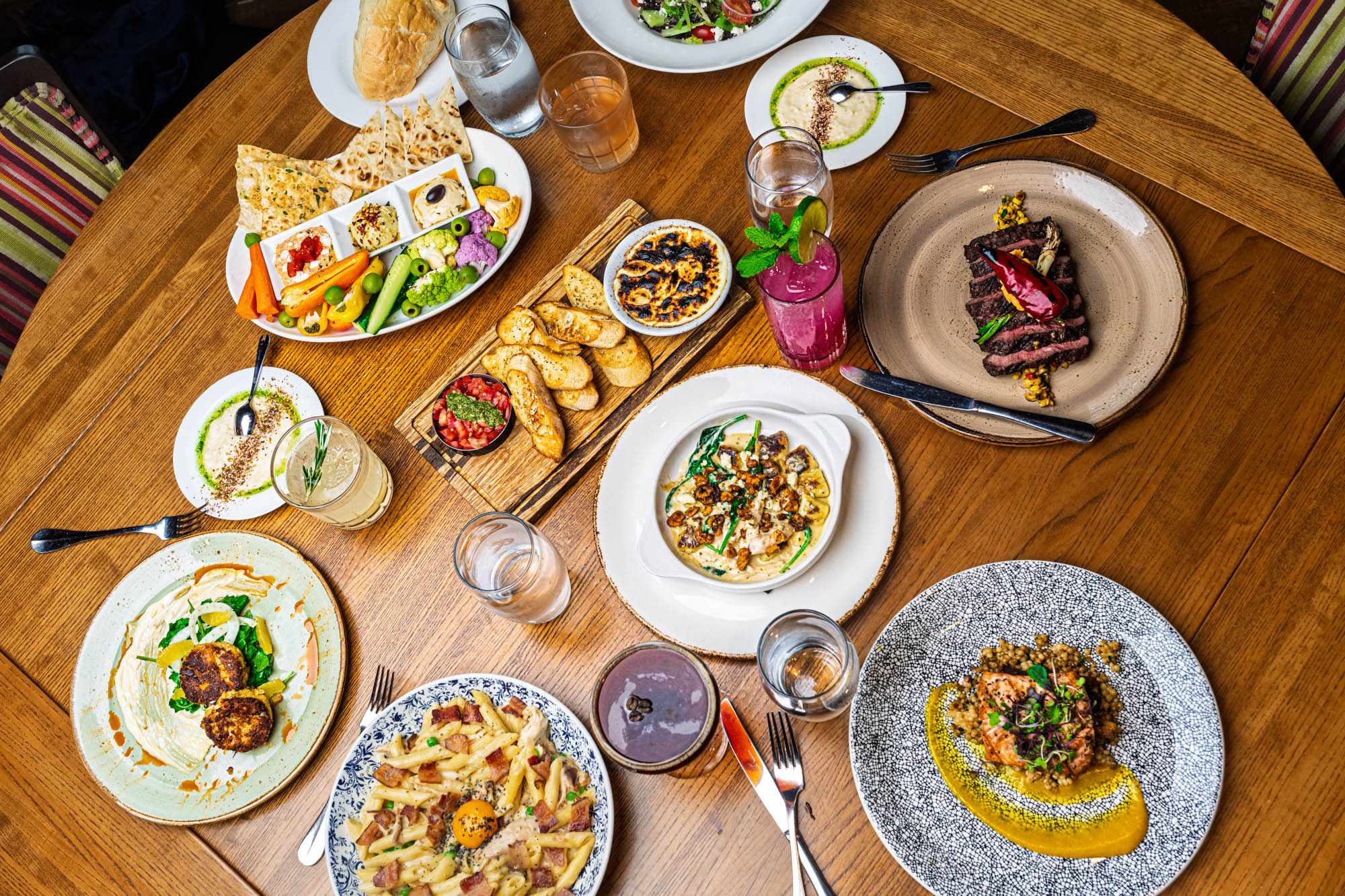 Table spread with an assortment of food plates and drinks, overhead shot