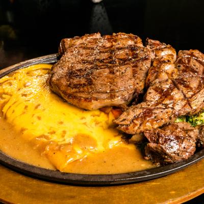Ribeye steak served in cast-iron skillet with enchilada covered in cheese sauce.