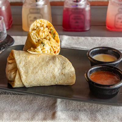 Halved burrito served with two sauces on a dark plate.