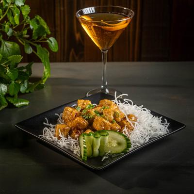 Sesame tofu served with noodles and cucumber slices, accompanied by a cocktail.