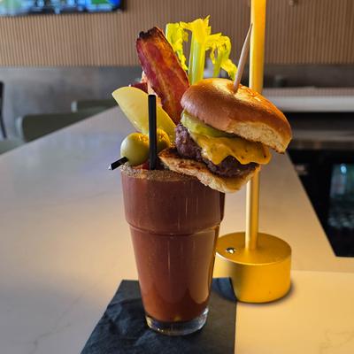 Bloody Mary cocktail topped with a cheeseburger slider, bacon, and celery.
