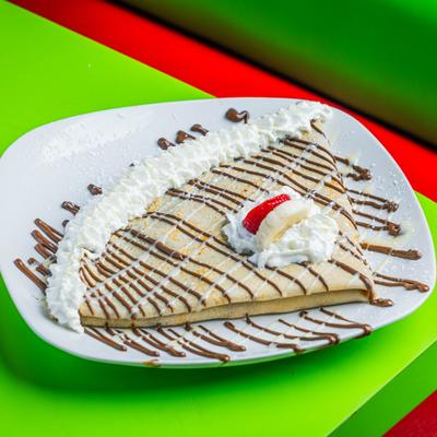 Strawberry Banana Crepe served on a plate drizzled with chocolate.