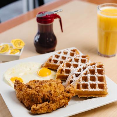 Chicken and waffles with sunny-side-up eggs a glass of orange juice.
