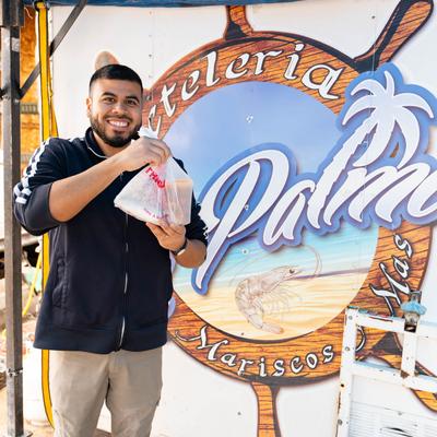 A customer holding a bag with food to go in front of a wall logo.
