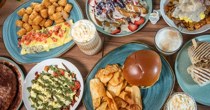 Assorted breakfast dishes with coffee drinks, pastries, and burger on a wooden table