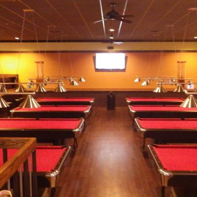Rows of red pool tables under hanging lights inside a wooden hall.