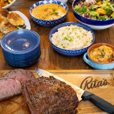 Cut of roast beef on a cutting board alongside various side dishes in blue bowls.