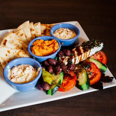 Three types of hummus, cucumbers, olives, feta cheese, served with pita bread