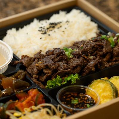 Beef bulgogi lunch box with rice, veggies, and sauces.